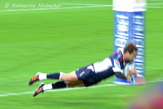 Und da fliegt er über die Linie....... "Yeaaaaah", wird laut gerufen und die Fans um mich herum jubeln und freuen sich. Es war ein glücklicher, einfacher Gewinn, für den sie 5 Punkte bekamen (sie haben den Ball über die Linie getragen, was ein "Try" ist). Danach dürfen sie noch einmal von einem beliebigen Punkt auf das H-förmige Tor schießen und bekommen dafür 3 Punkte.