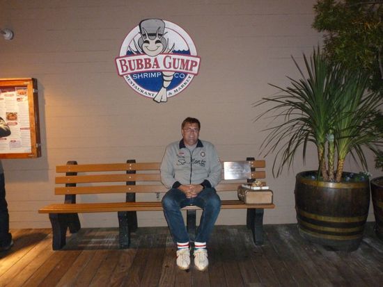 Die Forest-Gump-Bank aus dem Film mit dem Koffer und der Pralinenschachtel. In die Sportschuhe aus Kunststoff kann man seine eigenen Füße stecken und sich so kurz in Forest Gump verwandeln.