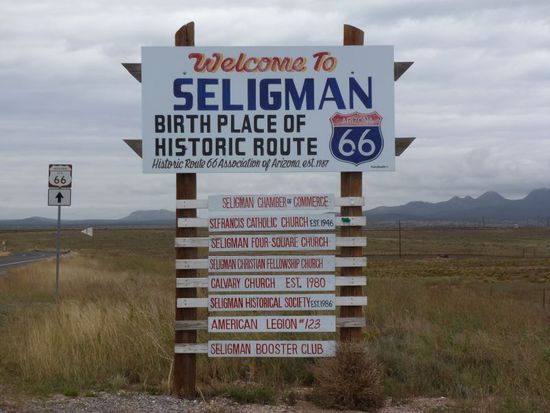 Nach 1 1/2 Stunden ist es soweit - wir biegen von der langweiligen Interstate endlich auf die Route 66.
Mir stehen jetzt schon Tränen in den Augen, weil ich totaler Fan bin und schon Jahre davon träumen hier zu fahren.
Ich springe auf meinem Sitz herum vor Ungeduld.
Denn heute möchte ich mein Idol treffen - Angel Delgadillo - dieser heute 84 Jahre alte Herr ist dafür verantwortlich dass es die Route 66 überhaupt noch gibt und befahrbar ist.
Er lebt sein Leben lang schon in Seligman, einem typischen Route66-Dorf, sein Vater hatte dort schon seinen Friseur und Barber-Laden, er übernahm dann das Geschäft in jungen Jahren.
Manchmal rasiert er noch in guter alter Manier wie man in den alten amerikanischen Filmen manchmal noch sieht.
In seinem Laden scheint die Zeit stehengeblieben zu sein, es ist heute Museum, Andenkenladen und Barber-Shop zugleich.
Er sammelt Autokennzeichen aus aller Welt, wir haben ihm extra ein ganz besonderes mitgebracht über den großen Teich.
Denn unser Kennzeichen AZ ist gleichzeitig das Kürzel des US-Staates Arizona, in der Angel ja lebt.
Wir sind gespannt was er sagt und ob er sich freuen wird.