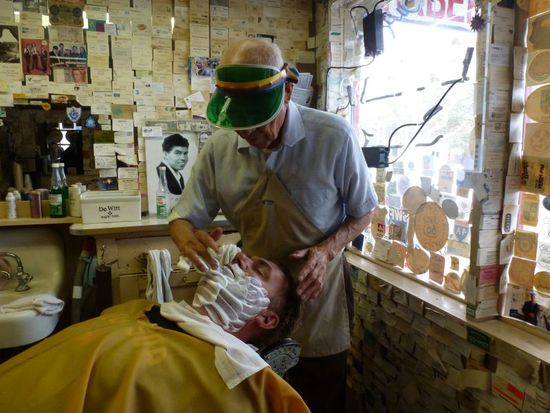 Dann bittet er uns herein und Bernhard legt sich auf den alten, schon zerschlissenen 50ziger Jahre Rasierstuhl, Angel setzt sich seine berühmte obligatorische Mütze auf die er immer beim rasieren trägt und los geht es.
Es sieht aus wie in einem alten Film weil die Umgebung perfekt ist.
Wir unterhalten uns mit ihm und dauernd kommen mal wieder Fans herein und fragen ob sie ein Foto machen dürfen.
Bernhard ist jetzt wahrscheinlich in Dutzenden Urlaubs-Fotoalben in der ganzen Welt zu sehen - auch in Japan 