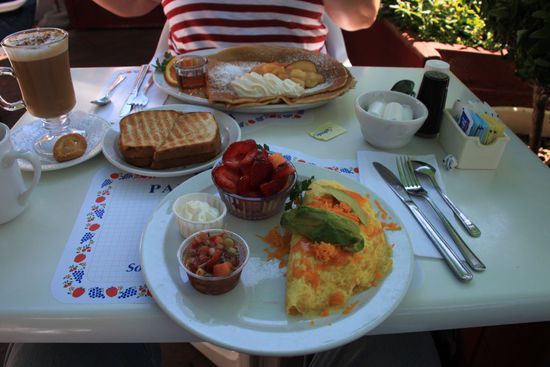 Unser Essen kommt und sieht total lecker aus.
Bernhard hat ein California Omelett mit Salsa und einem Schälchen frischen Früchten mit Sahne.
Ich habe einen Pancake mit Zimt-Äpfeln und Sahne.
Wir lassen es uns schmecken.
Leider lockt der süße Geruch die Bienen an und dann passiert eine irrsinnig komische Sache.
Ich will euch das nicht vorenthalten.
Als wir da so sitzen und essen kommen dauernd Bienen an.
Wir wedeln mit einem kleinen Werbeaufsteller und den Servietten herum und verscheuchen die Viecher.
Einmal waren vier oder fünf Bienen da und ich wedelte hektisch mit meinem Messer herum, auf diesem klebte Sahne.
Durch das heftige Bewegen löste sich ein Teil davon und flog durch die Luft.
Hinter uns saß ein amerikanisches Paar und dem Mann klatschte die Sahne mitten auf den Hinterkopf.
Da er mit dem Rücken zu uns saß hatte er das mit dem Messer nicht gesehen.
Er fasste sich an den Hinterkopf und schaute dann seine Hand an und sah sich die Sahne an.
Nun schaute er in den Himmel und dachte ein Vogel hätte im auf den Kopf gemacht.
Da wir nicht auf uns aufmerksam machen wollten durften wir nicht lachen und ganz ernst bleiben.
Ihr könnt euch vorstellen wie schwer das war.
Aber als Bernhard sagte: Die weiße Sahne ist mitten in seinem schwarzen Haupthaar gelandet konnten wir uns dann doch nicht mehr halten.
Es war einfach so eine Situationskomik da drin.
Der Mann saß da und der Sahnefleck auf seinem Hinterkopf wurde langsam blasser.
Wir bezahlten schnell und ging davon um endlich anständig lachen zu können.
Das war dann der ganze Tag ein Running Gag bei uns.