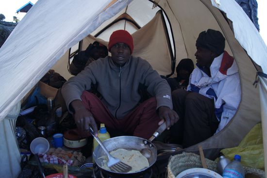 Abdallah in sienem Schlaf- und Kochzelt. Heute gibt es zum Frühstück frisches Chapati-Brot, dazu Rührei, Marmelade, Kaffee, Tee