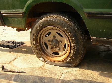 Doch als er losfahren will, entdeckt er, dass sein Auto einen Platten hat. Er flucht und schimpft und macht sich schließlich daran, den Reifen zu wechseln.