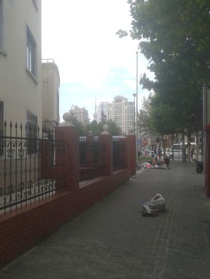 Ein noch deutlicheres Beispiel. 
Im Hintergrund der weltbekannte Fernsehturm (oriental pearl tower), das Wahrzeichen von Shanghai schlechthin. 
Vorne liegt ein (vermutlich Obdachloser) regungslos mitten auf dem Buergersteig...