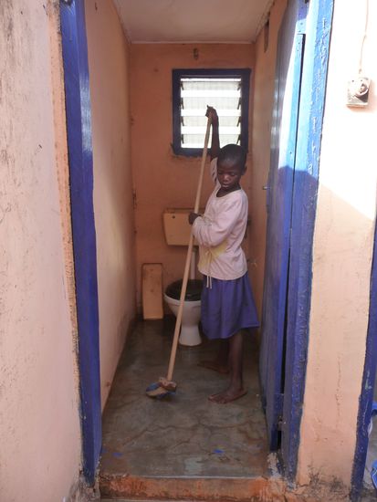 Vida reinigt gerade die Toilette - alles wie zu Hause - nur dass die Spülung nicht funktioniert (da es kein fließendes Wasser gibt) - man schüttet einfach einen oder zwei Eimer Wasser in die Toilette ...