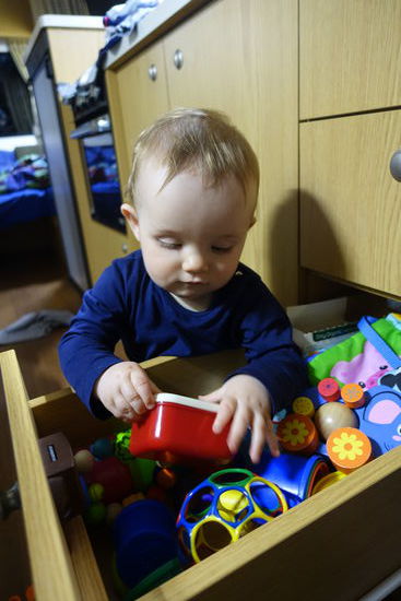 Emil erkundet stehend seine Spielzeugschublade. Am interessantesten fand er sein Fläschchen und seine Keksdose 