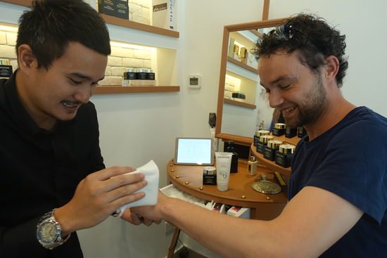 So zärtlich und gründlich wurden  Lars Hände noch nie zuvor bearbeitet.
Sehr geschickt wurde Lars von diesem Mitarbeiter in der Mall angesprochen und beraten. Uns ist der Laden auf dem Weg zum Ausgang nicht einmal aufgefallen, da uns das eigentlich auch nicht interessiert. Ruckzuck saßen wir auf zwei Hockern ( Ich habe schon zu Emil gesagt, er solle mal anfangen zu schreien, dann hätten wir einen guten Grund gehabt zu gehen.) Der müde Emil schrie nicht. Der Verkäufer konnte in Ruhe seine Wundercremes, die sämtliche Hautprobleme heilen sollen, an Lars Handrücken ausprobieren Nein, wir haben letztendlich keine der Cremes für 500 Dollar gekauft und auch nicht das Super Angebot 3 für 2 für 166$. Falls wir es uns doch noch anders überlegen, gäbe es auch die Firma ÉLévatione noch in London. Wenn wir noch in Singapur kaufen und dort registriert sind schicken Sie uns Nachbestellungen auch frei Haus. Wow!!!