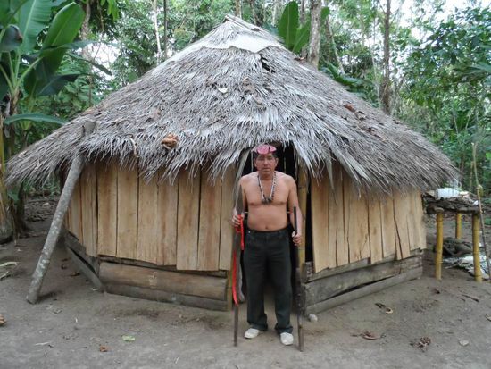 Alejandro mit Lanze und Gewehr vor seiner Huette die er fuer shamanistische Rituale nutzt