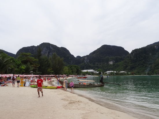 Strand auf Koh Phi Phi. Wie man sieht, sind überall Liegestühle und der Strand ist voll. Zwischen den beiden Strandseiten sind Geschäfte, Hotels und Restaurants.
