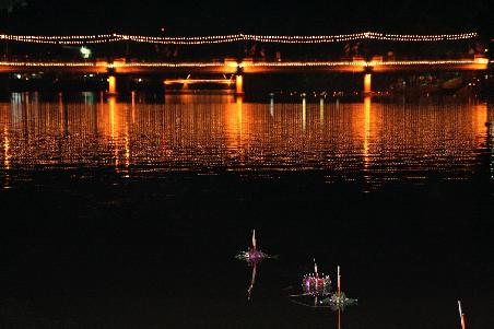 kleine loi krathong bananenblaetter-boote vor der beleuchteten bruecke
