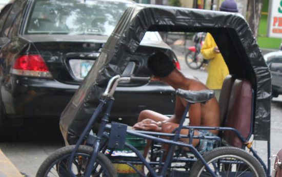 In den Strassen von Manila. Fahradtaxi. Der Junge Mann hat noch ein Eimer mit Wasser in seinem Fahrrad und ist dabei sich zu waschen.