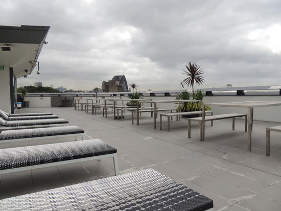 Die Dachterrasse mit Liegen und Stühlen. Im Hintergrund ist die Habour Bridge zusehen