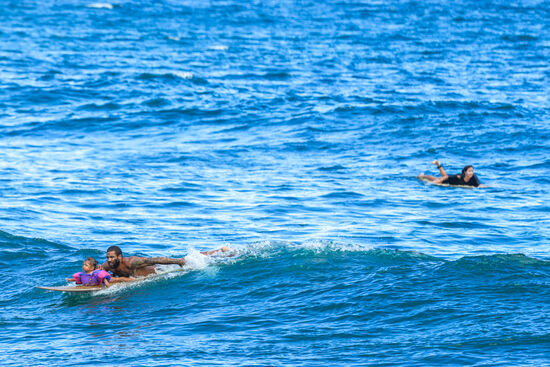 Hier sind die beiden zu sehen: er paddelt in die Wellen und dann lassen sie sich zurück zum Strand „tragen“ Obwohl die Wellen teilweise sehr hoch sind, bekommen sie kaum Wasser ins Gesicht—erstaunlich!