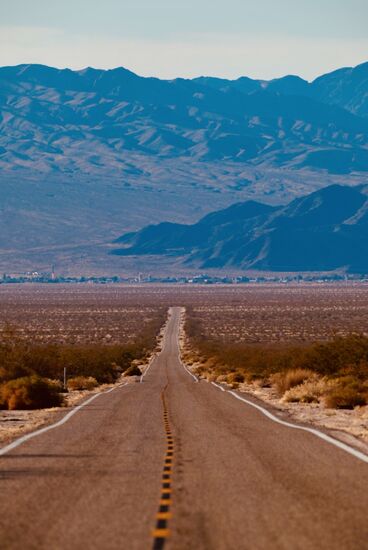 Es geht weiter Richtung Las Vegas. Weit im Hintergrund vor den Bergen liegt die Stadt Baker. Was glaubt Ihr, aus welcher Entfernung der Fotograf dieses Bild der Straße und Stadt gemacht hat? Es sind noch unglaubliche 10 Meilen/16 Kilometer bis nach Baker. Dabei sieht es so nah aus.