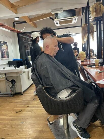 Inzwischen nimmt die Frisur von Thomas Form an…
Der junge Mann war zuerst etwas unsicher und die Chefin von der Anmeldung kommt öfter zur Kontrolle—aber mit der Zeit taut er auf und versucht sich in der Kommunikation.
Das Endergebnis muss dann auch von der Chefin abgenommen werden