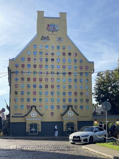 Auf dem Weg zum Bootsanleger sehen wir dieses Gebäude, welches ein Teil der Jakobskasernen ist. Diese wurden im 17.Jhd für schwedische Soldaten erbaut, die die Stadt verteidigen sollten. Heute befinden sich in den Kasernen Geschäfte, Cafés, Restaurants etc.
An der Fassade sind Wappen fast aller lettischen Städte und Gemeinden angebracht
