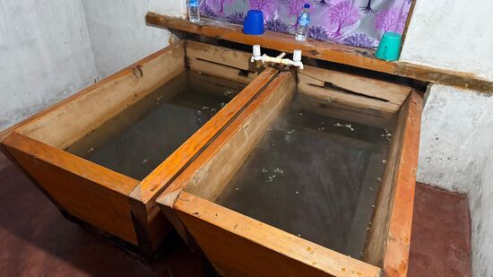 Anschließend gönnen wir uns noch ein sogenanntes „Hot Stone“ Bad in der mit Kräutern gefüllte Holzwanne—das Fußende geht außen weiter -dort wird das Wasser mit heißen Steinen erwärmt und fließt dann durch den Schlitz in die Wanne, in der man liegt—diese Angelegenheit ist mit 35 US$ nicht so ganz günstig
45 Minuten dürfen wir darin liegen, aber das reicht auch—uns wird mächtig warm-zwischendurch lassen wir 2x heiße Steine nachlegen.
Aus den Hähnen können wir kaltes Wasser zulaufen lassen
Dazu kommt er mit der Schubkarre an und läßt die heißen Steine am Fußende außen ins Wasser gleiten. Wir hören immer das laute ‚Zischen