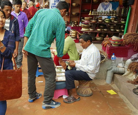 Wir gehen mit den Menschenmassen einmal um die Stupa und fangen viele verschiedene Eindrücke ein.
Hier sitzen Männer die Geld wechseln, damit die Leute Kleingeld für die Bettler haben.