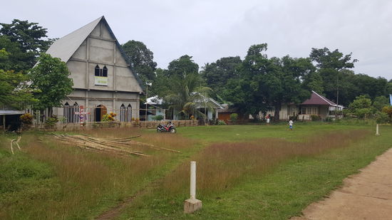 Im ersten Dorf -eine Kirche...? Davor mäht ein Mann mit einem Rasenkantenschneider die Rasenfläche