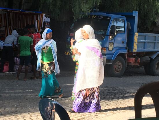 Gegenüber sind kleine Marktstände aufgereiht und hübsch gekleidete Frauen stolzieren die Straße hinauf