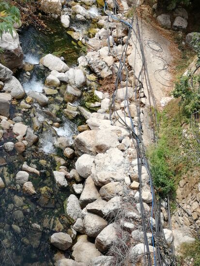 Wir fahren über eine Brücke unter der ein Gebirgsbach verläuft in dem die Stromleitungen kreuz und quer in dessen Bett offen mit verlegt wurden.