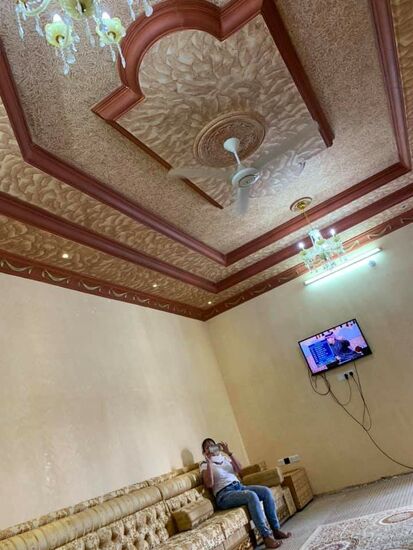 Ein riesiger Raum—eher ein Saal. Ringsum sind Sofas—Teppiche auf dem Boden, nur ein TV—sonst alles kahl
