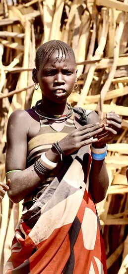 Eine besonders hübsche junge Frau. Das stählerne Halsband weist darauf hin, dass sie verheiratet ist. Kein anderer Mann darf etwas mit ihr anfangen. Tut er dass, hat das schlimme Folgen für ihn. 
Unverheiratete Frauen dagegen sind in dieser Kultur „Freiwild“. Die Frauen wissen das. Die meisten von Ihnen sind jedoch froh, wenn ein Mann sich für sie interessiert und heiraten möchte. Selbst als Nebenfrau. Denn wer sie heiraten will muss - je hübscher sie ist - viele Kühe und Ziegen an ihre Eltern geben.