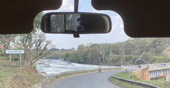 Und dieses Bild ist Auslöser einer Polizeiaktion. Weitere Fotos durften wir an dieser Stelle nicht mehr machen.
Ich habe mit Handy und Thomas mit Fotoapparat aus dem fahrenden Fahrzeug heraus fotografiert. Diese Brücke überbrückt den Nil in der Nähe der berühmten „Murchioson Falls“. Direkt hinter der Brücke wurden wir von einem Polizisten gestoppt. Denis fährt an den Straßenrand und uns ahnt böses. Ein Polizist kommt an den Wagen und erklärt, dass fotografieren dieser Brücke verboten sei. Denis muss aussteigen und zu zwei seiner Kollegen gehen, um sich dort zu erklären.
Der erste Polizist beginnt mit uns einen Smalltalk, erklärt, warum man nicht möchte, dass fotografiert werde. Neben dem Bauwerk seien auch Gebäude des Militärs und die möge man nicht ablichten. Thomas bietet an, dass er die Aufnahmen löscht, doch der Polizist winkt ab. Wir sollen sie ruhig behalten, wir seien ja Touristen und wir würden sicherlich nicht die Aufnahmen anderweitig nutzen. Denis diskutiert immer noch mit den Kollegen unseres Polizisten. Thomas bittet mich, ihm zwei Bonbons zu geben, die dann an den Polizisten gehen. Er freut sich sehr und nimmt sie gerne an. Wir unterhalten uns noch nett. Plötzlich fragt er uns „do you have water?“  Ja, wir haben noch Wasser, zwar warm, aber immerhin Wasser. Thomas reicht ihm das Wasser, der Polizist schaut etwas erstaunt und sparsam - nimmt aber die Flasche Wasser. - Im Rückspiegel sieht Thomas wie Denis einem der Polizisten die Hand zustreckt. Es wird sich verabschiedet, Denis kommt zum Wagen zurück und steigt ein. Wir fahren los und Thomas fragt Denis, wieviel er bezahlt habe. Darauf sagt Denis: gar nichts. Ich habe ihnen gesagt, dass das nie wieder passieren werde. Versprochen! Und er habe ihm die Hand drauf gegeben. Darauf hin haben wir Denis gesagt, dass wir ihm eine Flasche Wasser gegeben haben, weil er darum gebeten hatte. He asked „do you have water?“
Denis fällt in schallendes Gelächter! „Do you have water means in Uganda do you have Money. He asked for Money.“ 
Ich habe schon oft von der korrupten Polizei in Afrika gehört—nun auch selber erlebt.
Dabei wäre es mir nicht mal bewußt gewesen
Immer wieder in den nächsten Stunden lacht Denis, schüttelt den Kopf und sagt „do you have water“.
