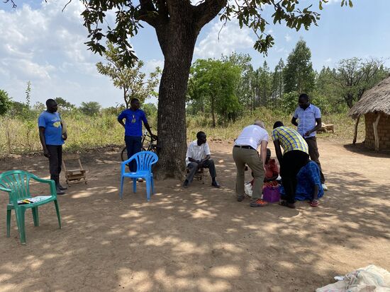 Im Schatten unter einem Baum sitzen Denis Mutter und eine der älteren Frauen, die wir unterstützen.