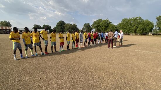 Aufstellung zum Anpfiff. Alle Spieler begrüßen uns mit Handschlag. Sogar ein richtiger Schiedsrichter ist vor Ort. Thomas lobt adhoc sein Original EM2020 Trikot aus: der Spieler, der das erste Tor schießt, bekommt es.