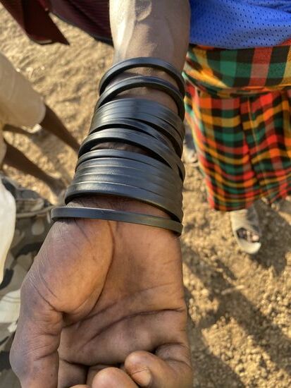 Uns fällt bei einem der Hirten auf, dass er sehr viele Lederarmbänder um den Arm trägt.
Wir fragen, was es damit auf sich hat.
Die Hirten sind häufig tagelang in der Steppe und sind dort allem ausgesetzt und ausgeliefert. Während sie die Tiere hüten sitzen sie auch auf dem Boden oder schlafen. Damit sie nicht von den Schlangen gebissen werden, tragen sie etwas aus Gummi. Schlangen mögen den Geruch von Gummi nicht. Hier, wo es sehr warm ist, entwickelt sich natürlich ein starker Gummigeruch. Das hilft und schützt sie