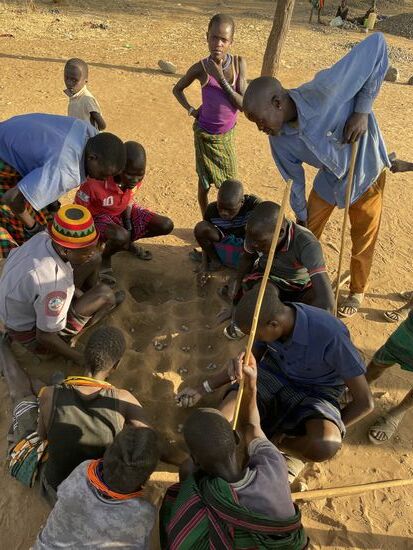 Ganz in der Nähe sehen wir einige Bewohner auf dem Boden sitzen bzw. knien. Hier findet ein „Brettspiel“ ohne Brett statt. Bis zu acht Spieler können hier spielen.