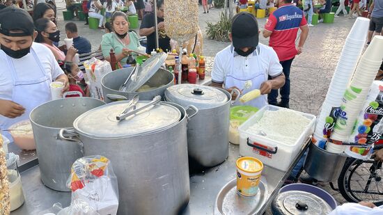 Irgendwas wird in einem Becher zusammen gemischt—es ist Mais mit Käse?