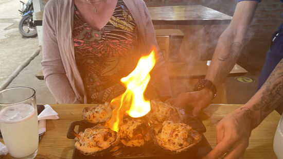 Ich bekomme Scampi und Tintenfisch mit Käse überbacken - in Muschelschalen serviert und flambiert.