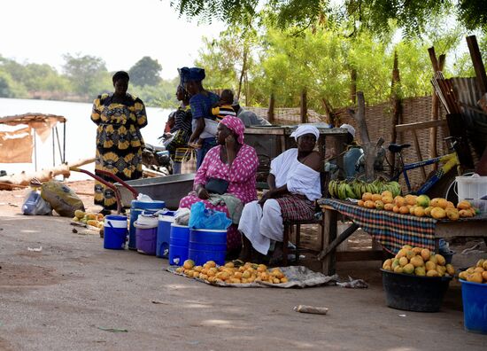 Die Frauen sitzen hier mit ihren farbenprächtigen Kleidern und Babies und verkaufen Obst und Gemüse