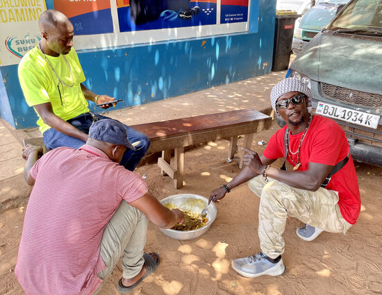 Einige der Fahrer haben sich eine große Schüssel mit Essen geholt: Reis und irgendwelche Blätter in Öl und Gewürzen. Dawda schnappt sich einen Löffel und haut erstmal tüchtig rein.