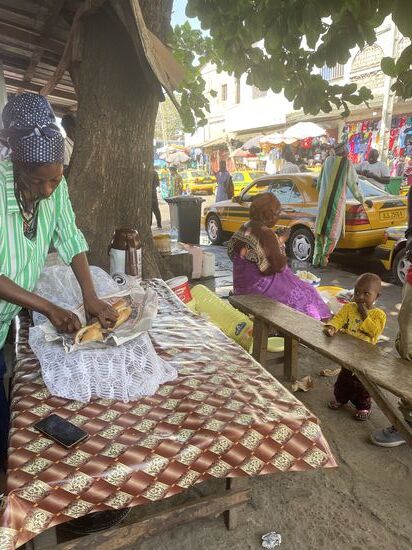 Ich laufe herum und sehe dann wie sich ein junger Mann ein Baguette belegen lässt.
In Erinnerung an das leckere Baguette von Dawda am ersten Tag, schaue ich mir das genauer an. Hier kommen Gurken und gebratener Fisch drauf, welchen die Dame aus  Teilen mit der Gabel von den Gräten kratzt und das Baguette damit belegt. Ich bestelle auch eines, lasse es in 3 Teile teilen und es wird in Zeitungspapier gepackt für später…