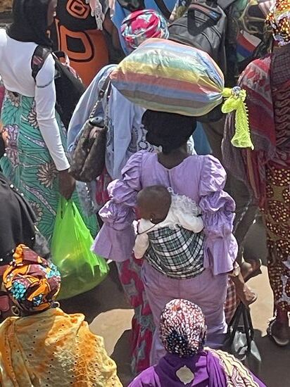 Frauen schleppen Säcke auf dem Kopf und haben die Kinder am Rücken