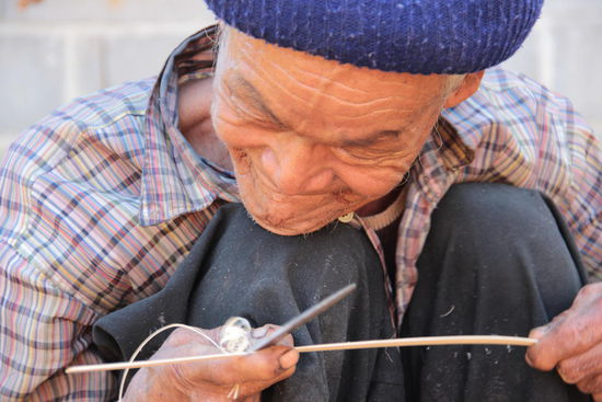 der alte Mann schnitzt in mühevoller Kleinarbeit, zarte Bambusstreben um daraus Körbe zu flechten...